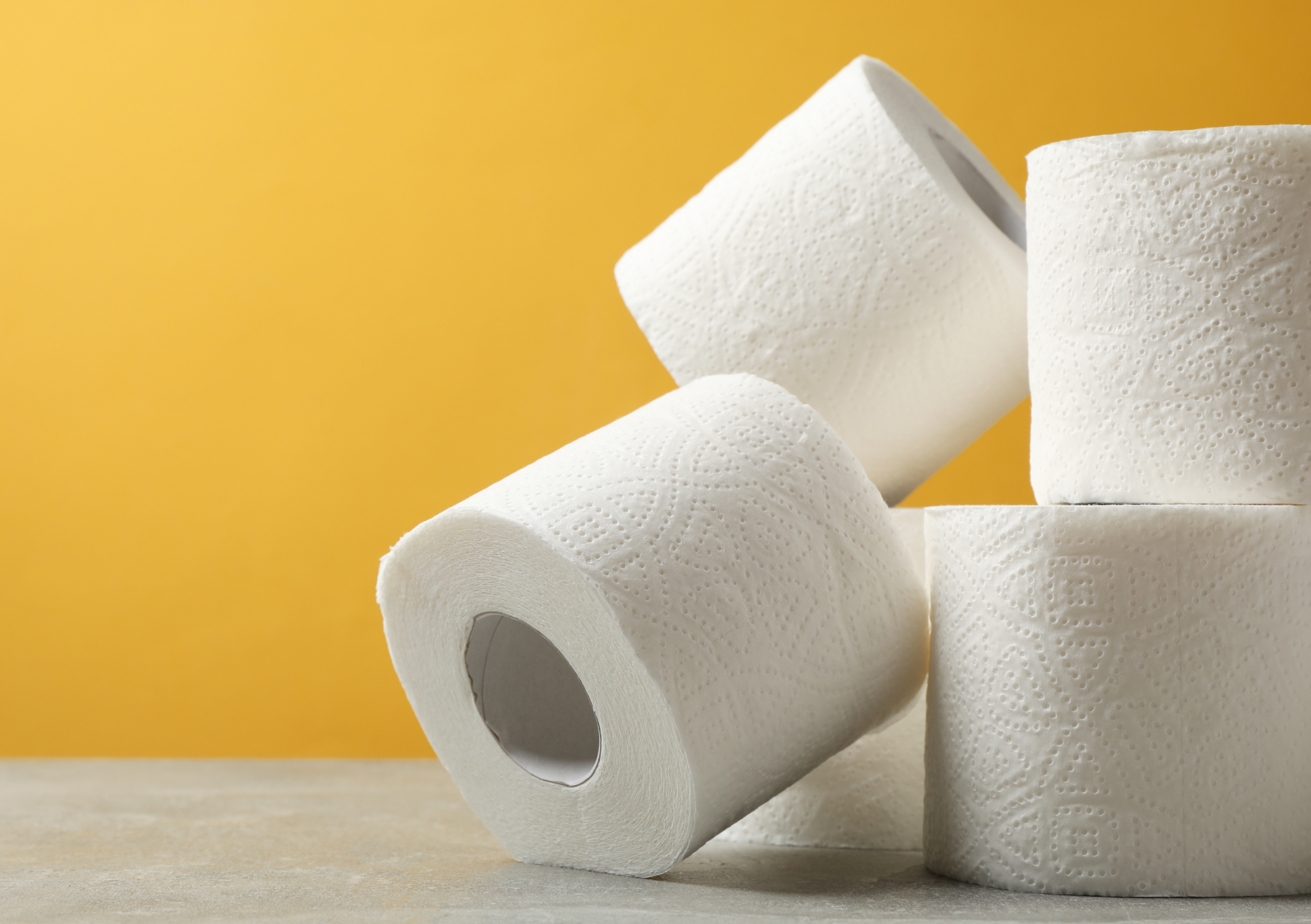 Four rolls of toilet paper stacked against a yellow background.