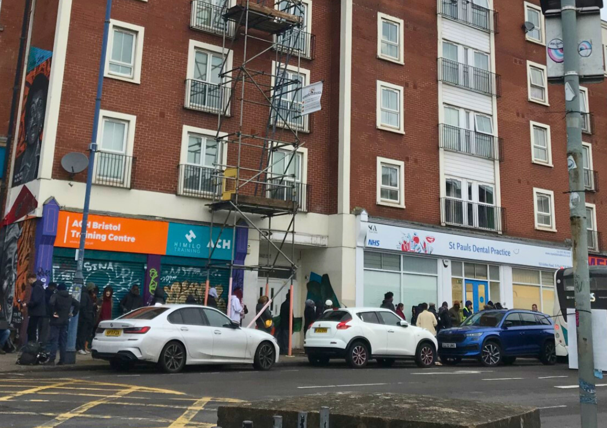 A queue of people in front of St Pauls Dental Practice, lining up on a street in St Pauls, Bristol.