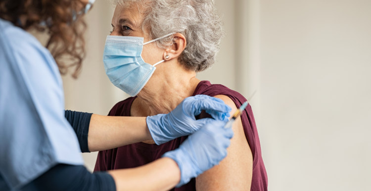 An older woman wearing a face mask receiving a vaccine.