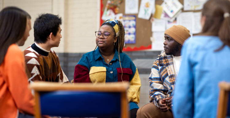 A diverse range of young adults sitting around a small table and having a group discussion.