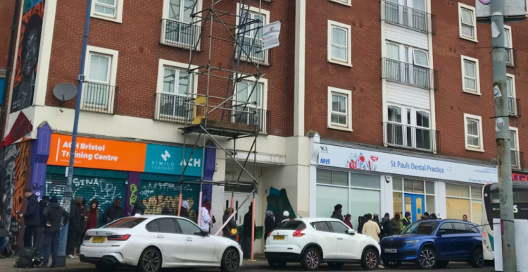 A queue of people in front of St Pauls Dental Practice, lining up on a street in St Pauls, Bristol.