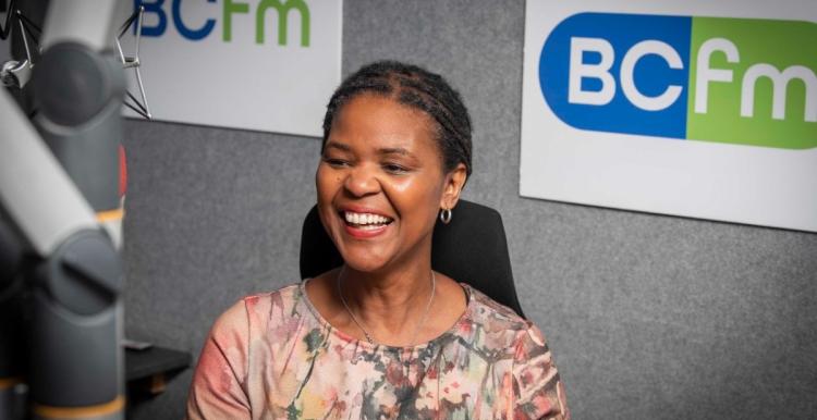 A woman smiling, sitting behind a microphone.
