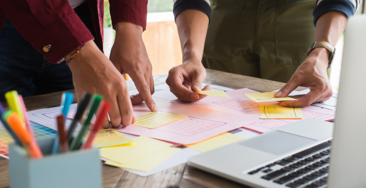 People arranging sticky notes and index cards on a desk.