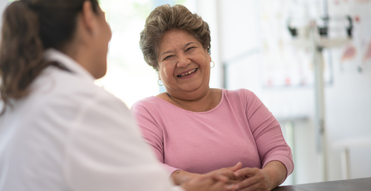 A woman speaking to a doctor. She is smiling and wearing a pink jumper.