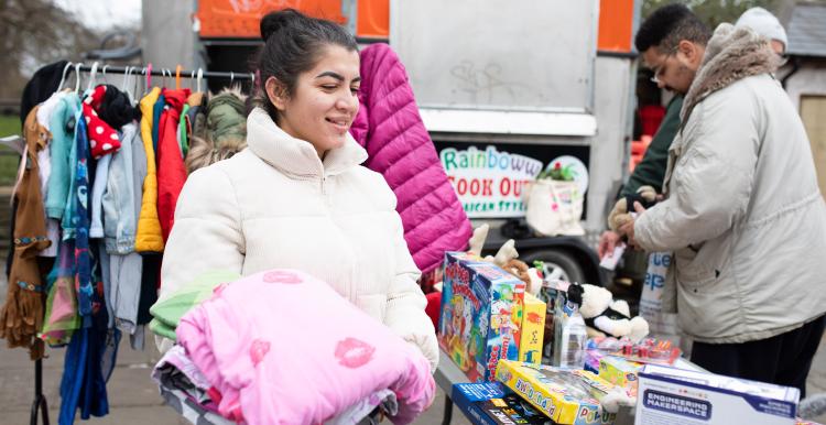 A woman at a stall in a market, carrying a pink blanket.