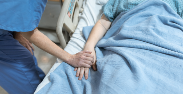 A nurse holding a patient's hand in a hospital bed