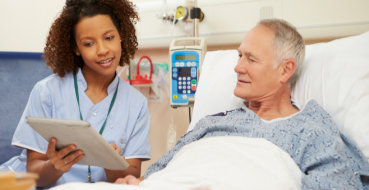 A man in a hospital bed, being shown something on a tablet by a member of hospital staff