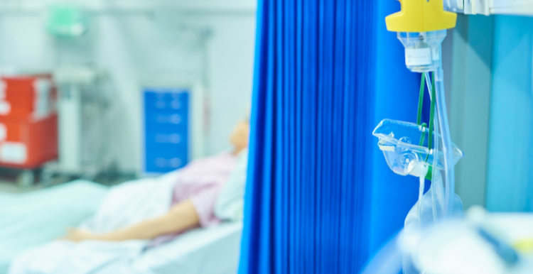 A person lying in a hospital bed, partially hidden by a blue hospital curtain