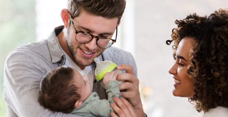 A father standing next to his wife, holding and feeding his baby