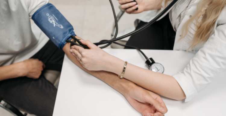 A person wearing a blood pressure cuff getting their blood pressure checked by a medical professional