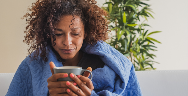 A woman with a blanket around her drinking a hot drink