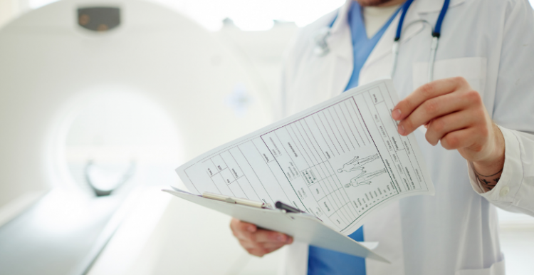 A doctor looking at some paperwork, standing in front of a CT scanner