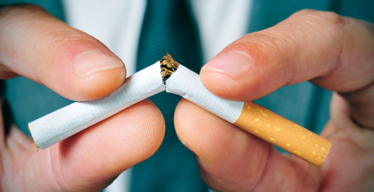 Close-up of a man wearing a suit snapping a cigarette in half with his hands