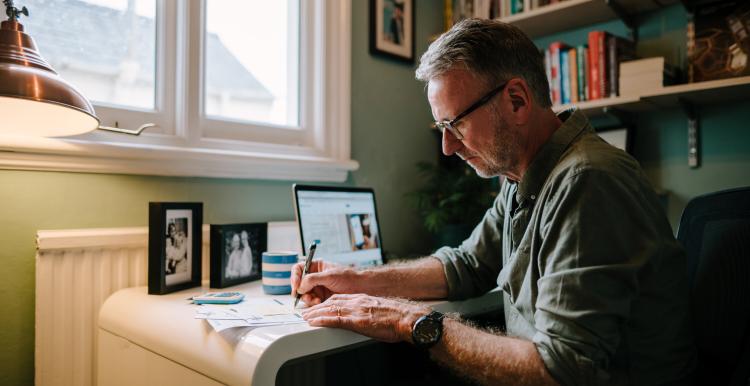 A man sitting at a desk with a laptop, taking notes