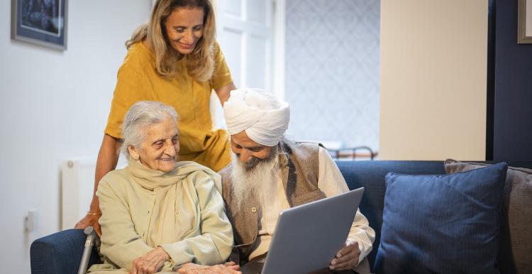 An older Sikh couple using a laptop with support from their daughter