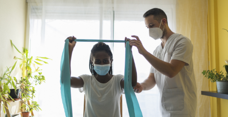 A medical professional helping a woman hold a piece of fabric between her hands, with her arms raised over her head