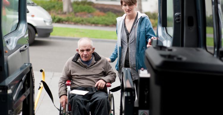 Man in a wheelchair being helped into a bus