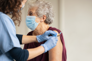 An older woman wearing a face mask receiving a vaccine.