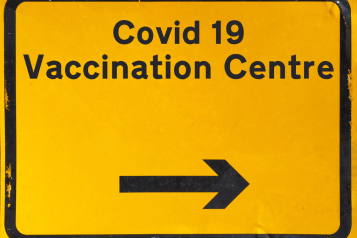 A yellow traffic sign directing people to a Covid 19 Vaccination Centre