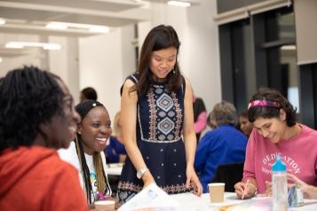 A diverse group of women sitting around a table, laughing and talking to each other.