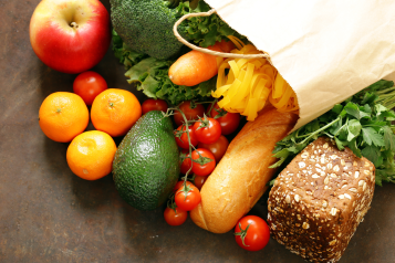 A paper shopping bag full of fruits, vegetables, bread and pasta.
