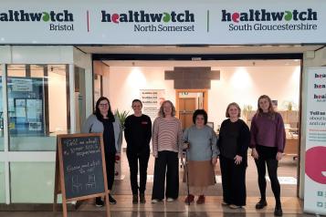 Five members of the Healthwatch team standing at the entrance to their new office under a sign for Healthwatch Bristol, North Somerset and South Gloucestershire.