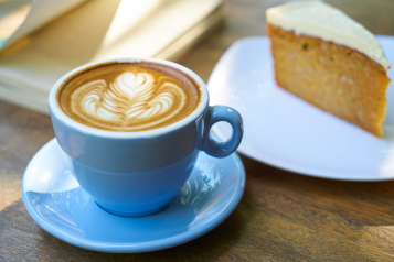 A blue mug of coffee and a slice of cake on a plate.