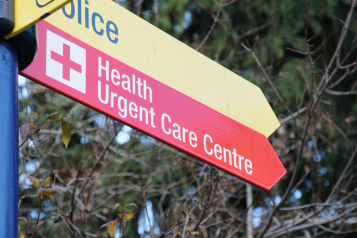 A red sign on a signpost pointing towards 'Urgent Care Centre'