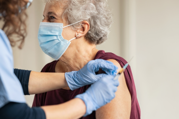 An older woman wearing a face mask receiving a vaccine.