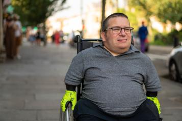 A man in a wheelchair, pushing himself along the pavement.