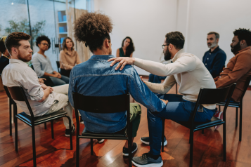 A group of men sitting in a circle, talking and showing support to each other.
