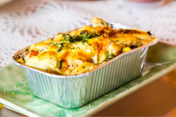 Lasagne ready meal in a foil container on a plate, on a table.