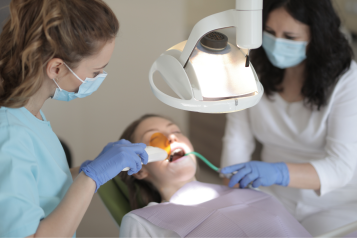 A patient lying on a dentists chair, receiving treatment from two dental professionals.