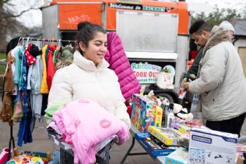 A woman at a stall in a market, carrying a pink blanket.