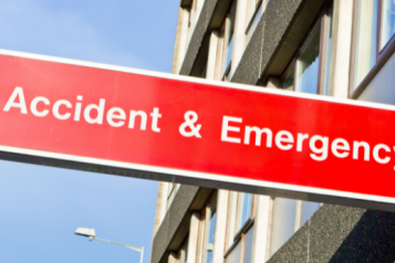 A thin, red, rectangular sign. The text, which is white, reads: Accident & Emergency. There is blue sky and a building in the background.