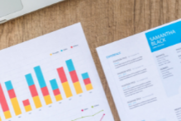 A laptop and sheets of paper showing bar graphs