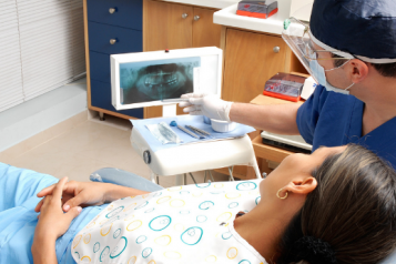 A woman in a dentist's chair, being shown an x-ray by a male dentist