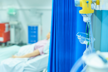 A person lying in a hospital bed, partially hidden by a blue hospital curtain