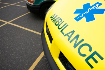 The front of a yellow ambulance, parked in a car park.