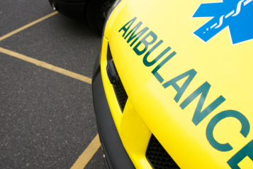 The front of a yellow ambulance, parked in a car park.