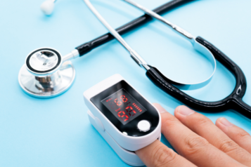 A pulse oximeter on someone's finger with a stethoscope in the background