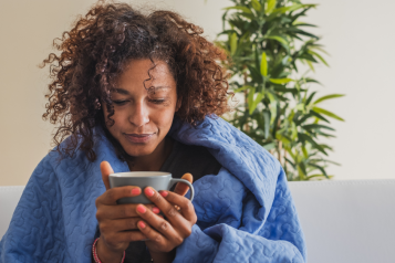 A woman with a blanket around her drinking a hot drink