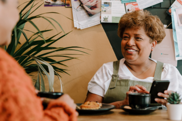 Two people sitting at a table. One is smiling and using her mobile phone.