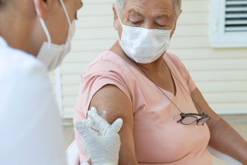 An older woman wearing a face mask receiving a vaccine