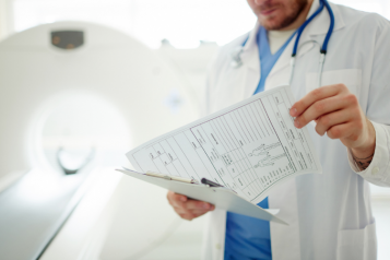 A doctor looking at some paperwork, standing in front of a CT scanner