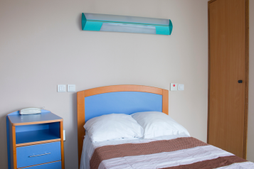 A hospital ward bedroom with a single bed, cupboard, and bedside table