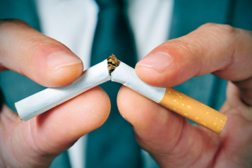 Close-up of a man wearing a suit snapping a cigarette in half with his hands