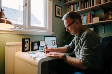 A man sitting at a desk with a laptop, taking notes