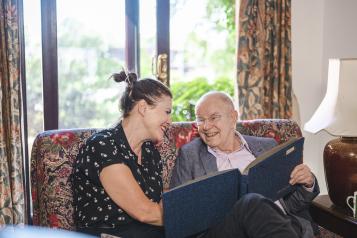 A woman and older man sitting on a sofa, looking at a photo album