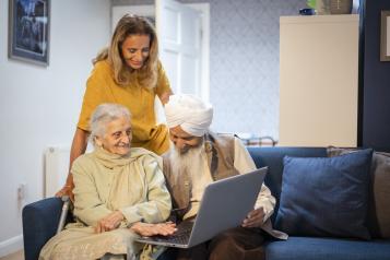 An older Sikh couple using a laptop with support from their daughter